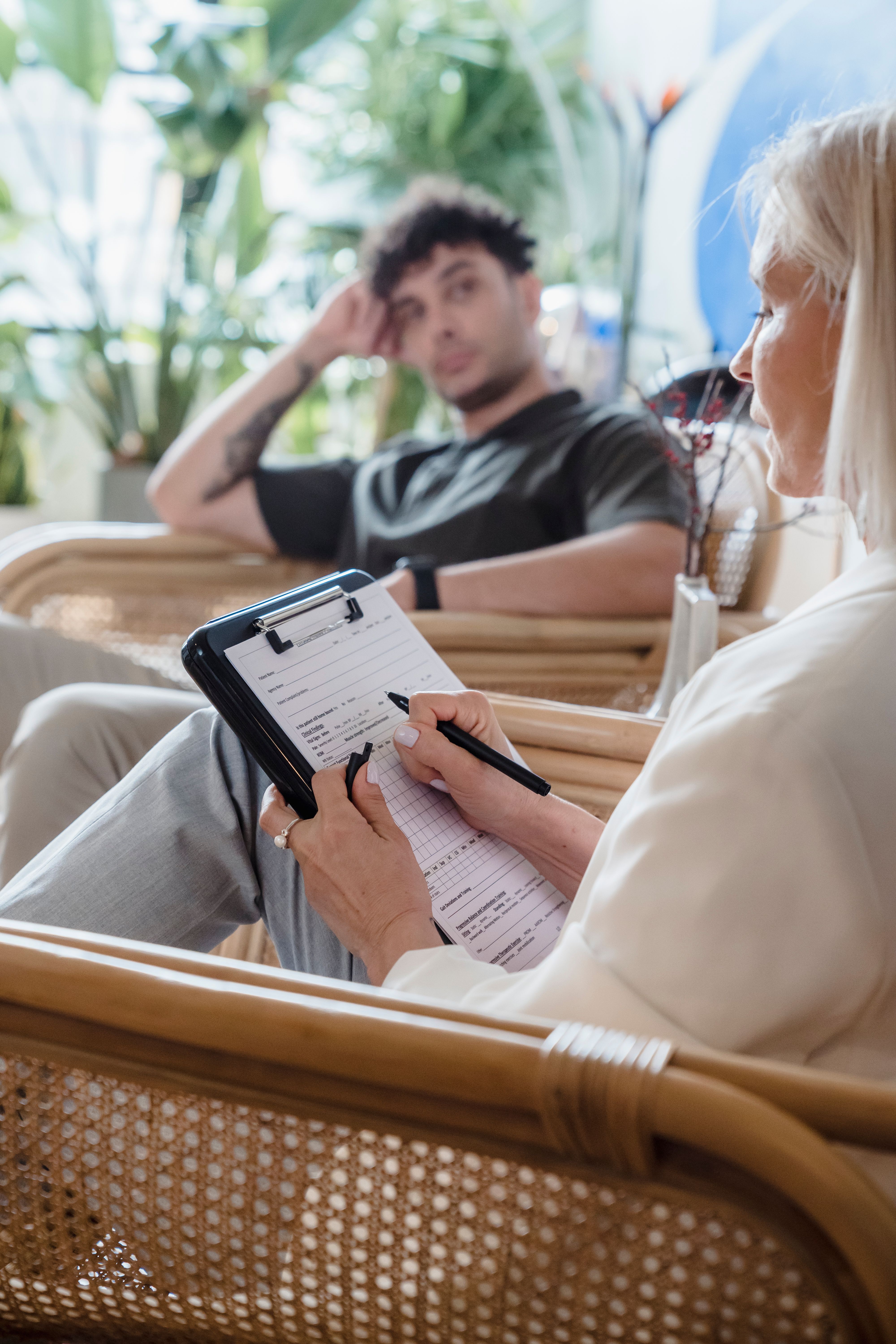 A professional taking notes on a clipboard while speaking with an adult seated opposite